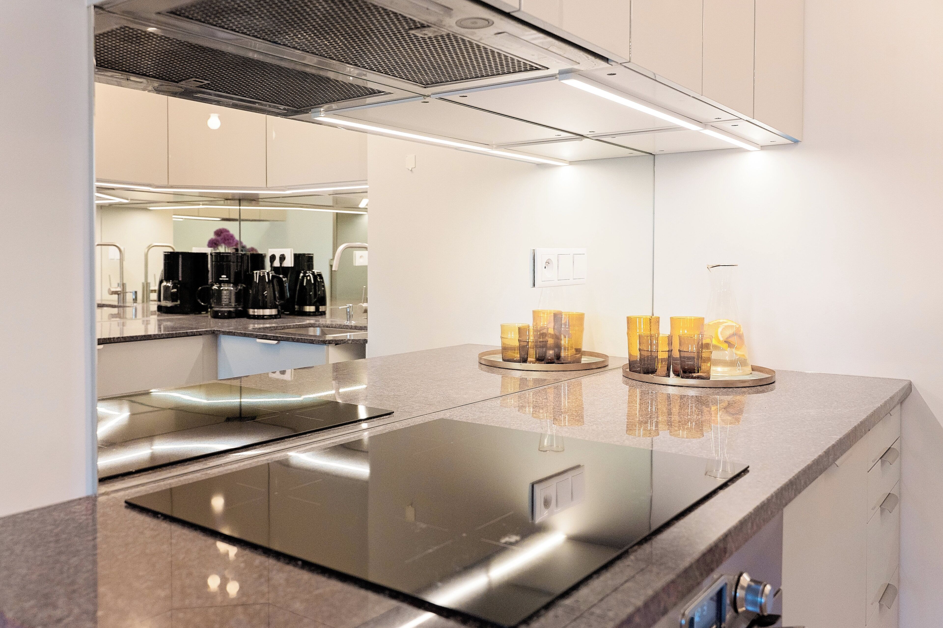 A modern kitchen with a sleek black induction cooktop, a stainless steel refrigerator, and a glass backsplash.