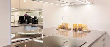 A modern kitchen with a sleek black induction cooktop, a stainless steel refrigerator, and a glass backsplash.