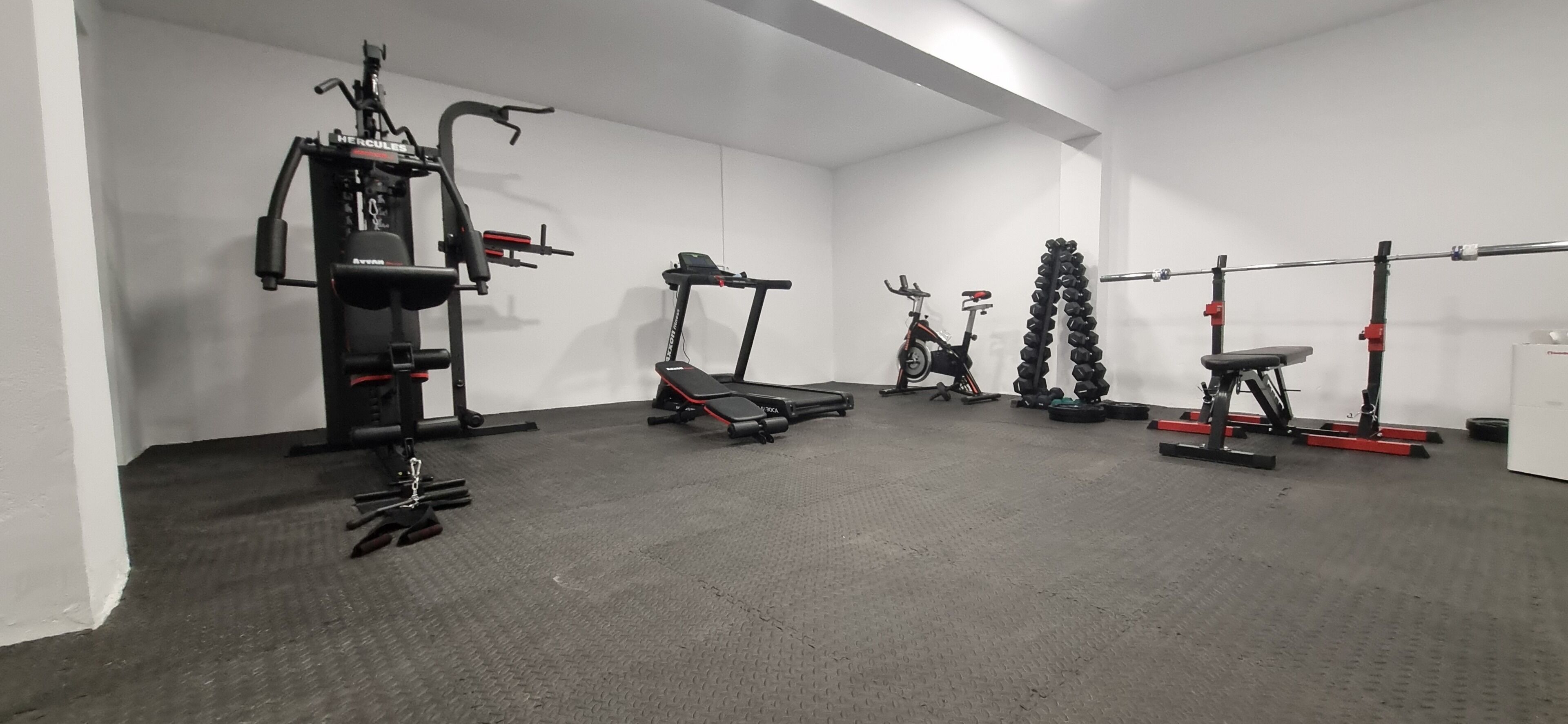 Een sportschool met cardioapparatuur, gewichten en een bank.