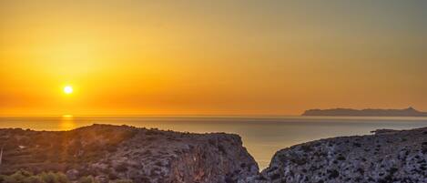 A coastal landscape with rocky terrain and a sunset over the sea.