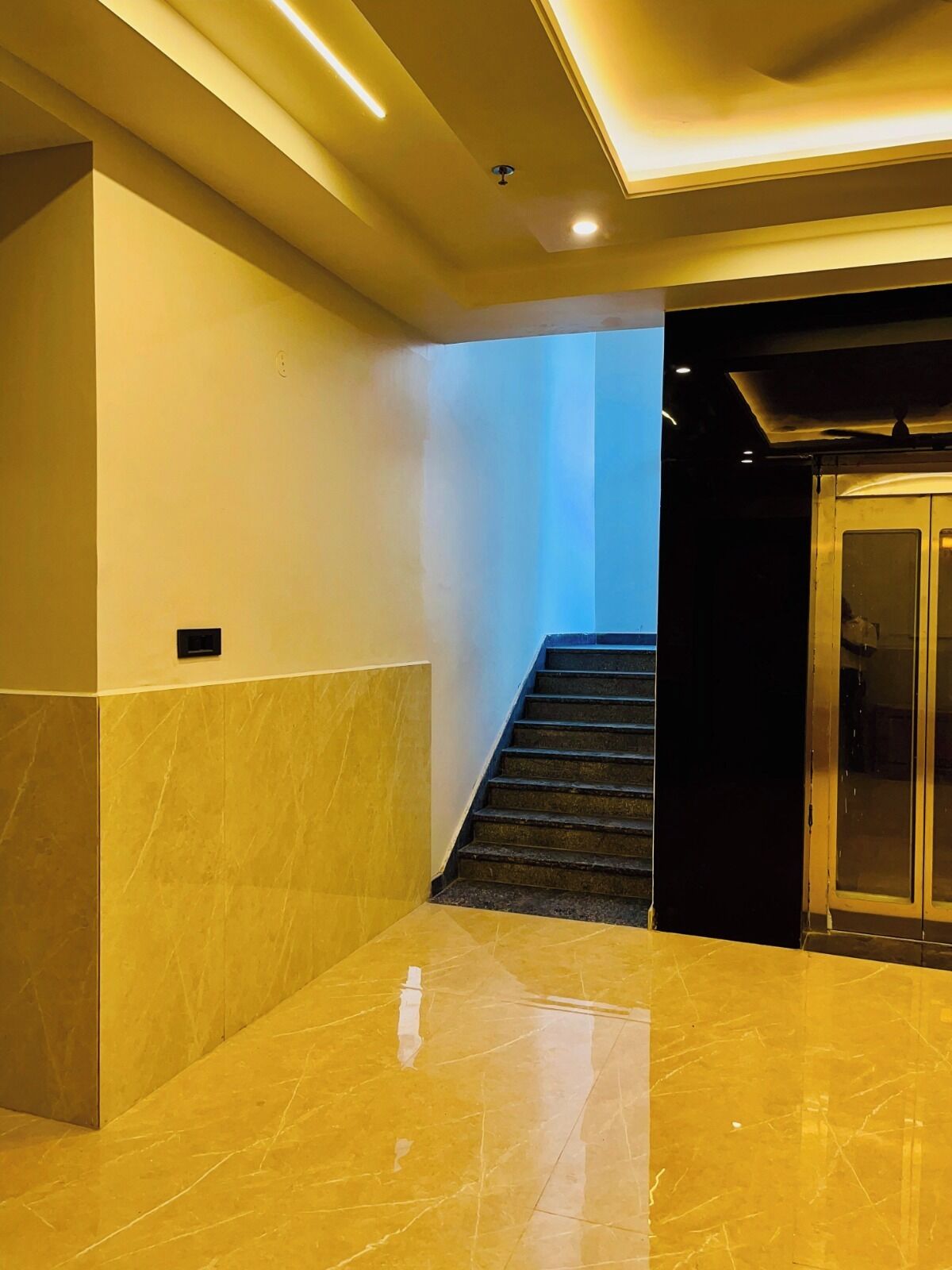 A modern interior with a marble floor, a staircase, and a glass elevator.