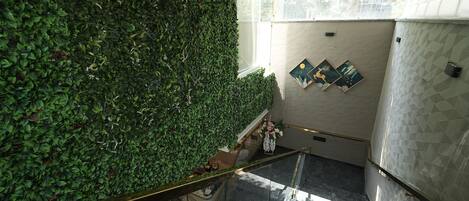A staircase with a glass railing, a wall covered in green foliage, and a tiled wall with geometric patterns.