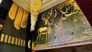A luxurious lobby with a marble reception desk, a chandelier, and a mural of a golden deer and tree.