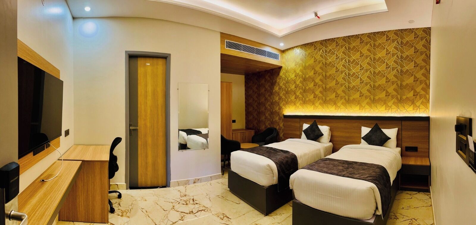 A hotel room with three beds, a desk, a TV, and a bathroom.