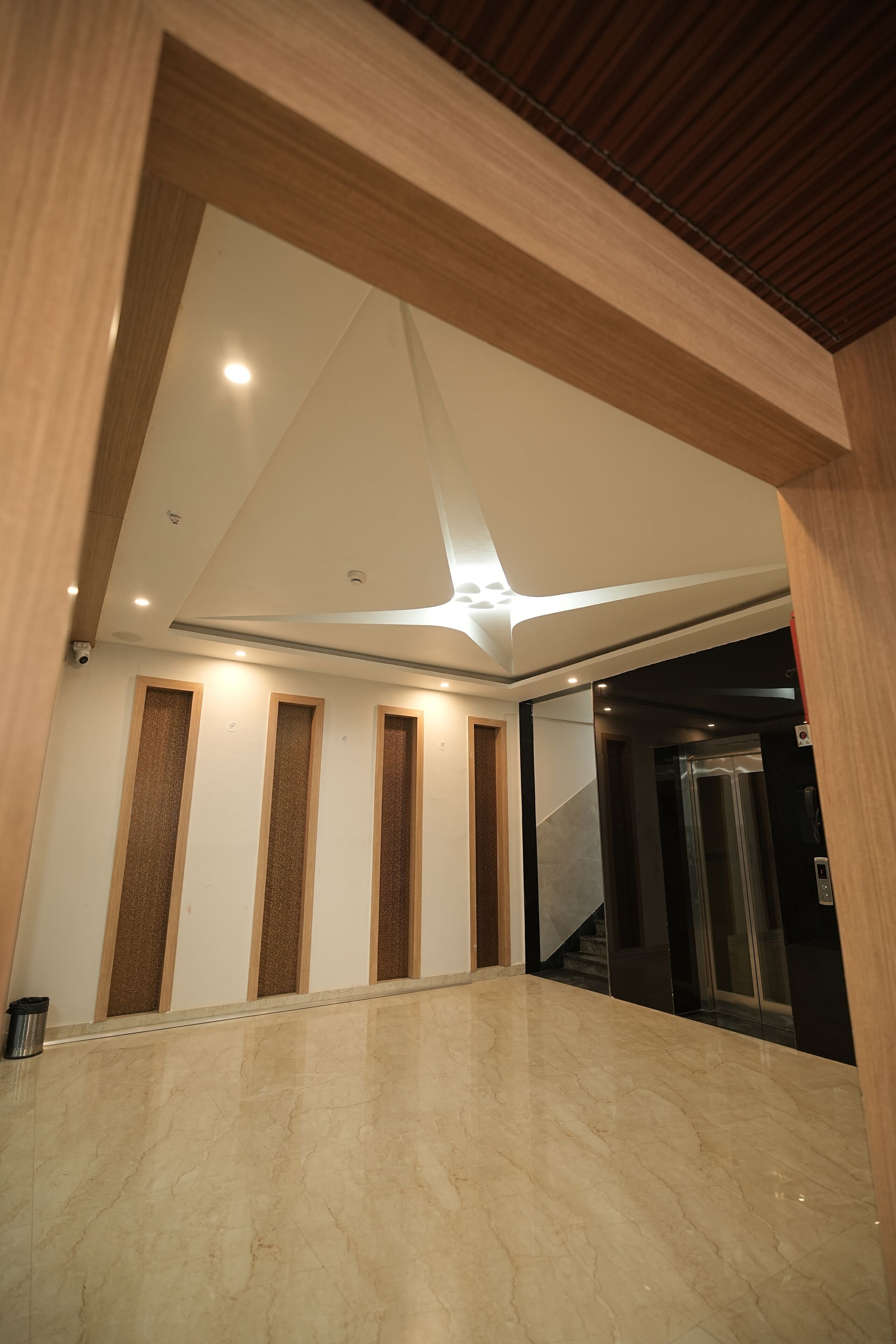 A modern interior with a marble floor, wooden panel accents, and a ceiling with recessed lighting.