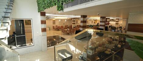 A modern hotel lobby with a glass staircase, a seating area, and a kitchen area visible in the background.