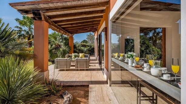 A covered outdoor dining area with a long table set for breakfast, surrounded by tropical plants and a wooden pergola. - Villa Pineta 6 Emma Villas (Castelvetrano)