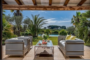 A patio with two grey sofas, a glass coffee table, and a view of a pool and greenery.