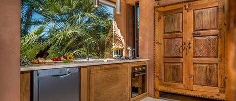 A kitchen with wooden cabinets, a dishwasher, and a window overlooking palm trees.