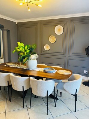 Un coin repas avec une table en bois, six chaises, une plante en pot et des assiettes décoratives accrochées au mur.