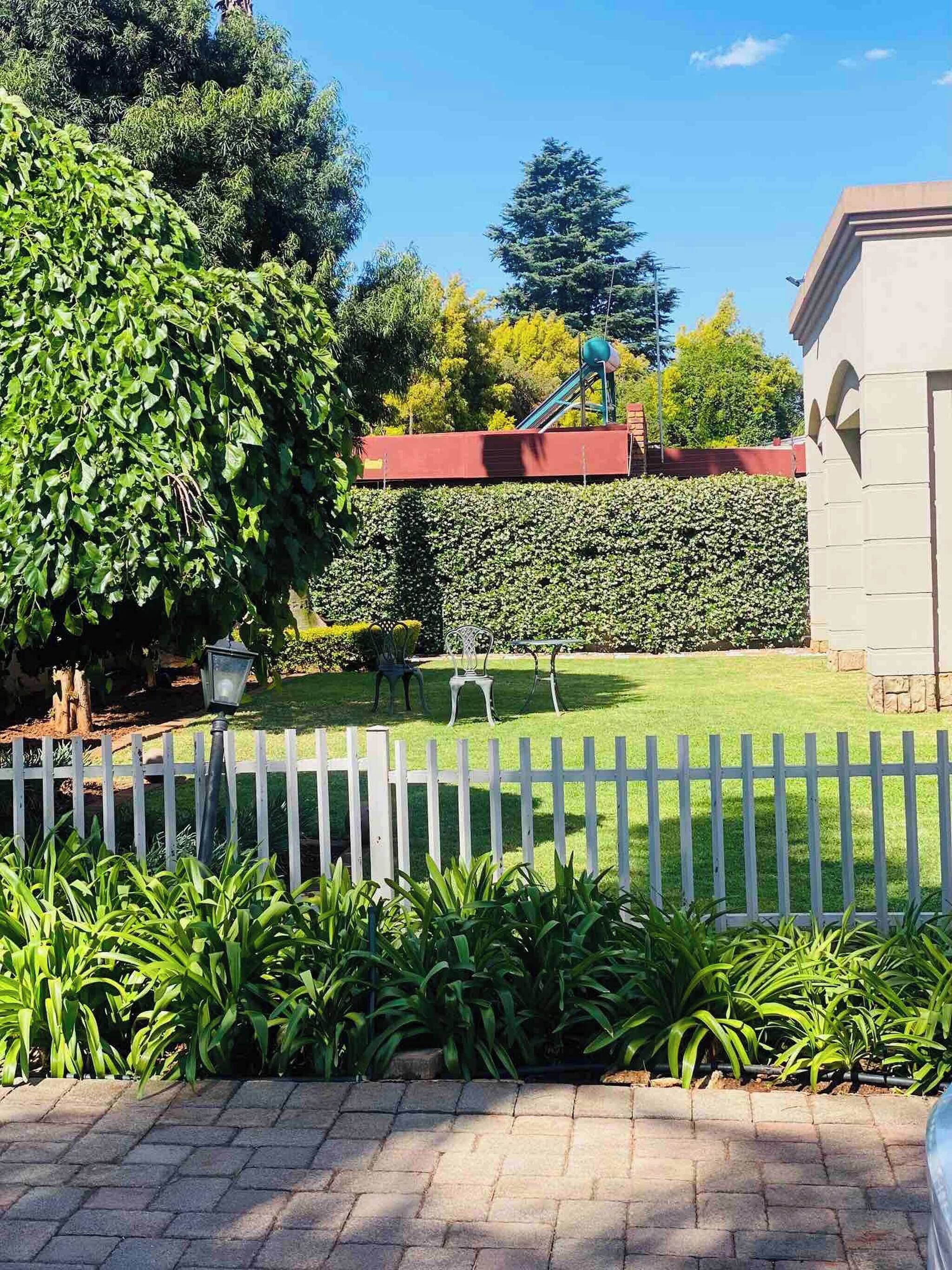 A well-maintained garden with a white picket fence, a paved walkway, and a variety of plants.