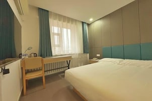 A hotel room with a bed, a desk, a chair, a window with curtains, and a nightstand.