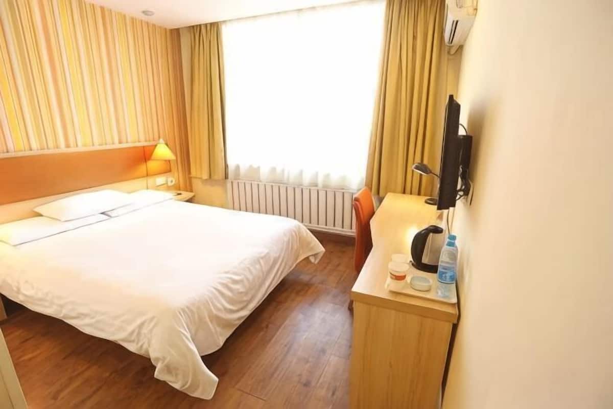 A hotel room with a bed, a desk with a chair, a TV, and a window with curtains.