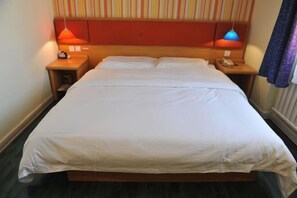 Habitació d'hotel amb un llit gran, dues taules de nit i un panell de capçaleri amb ratlles.