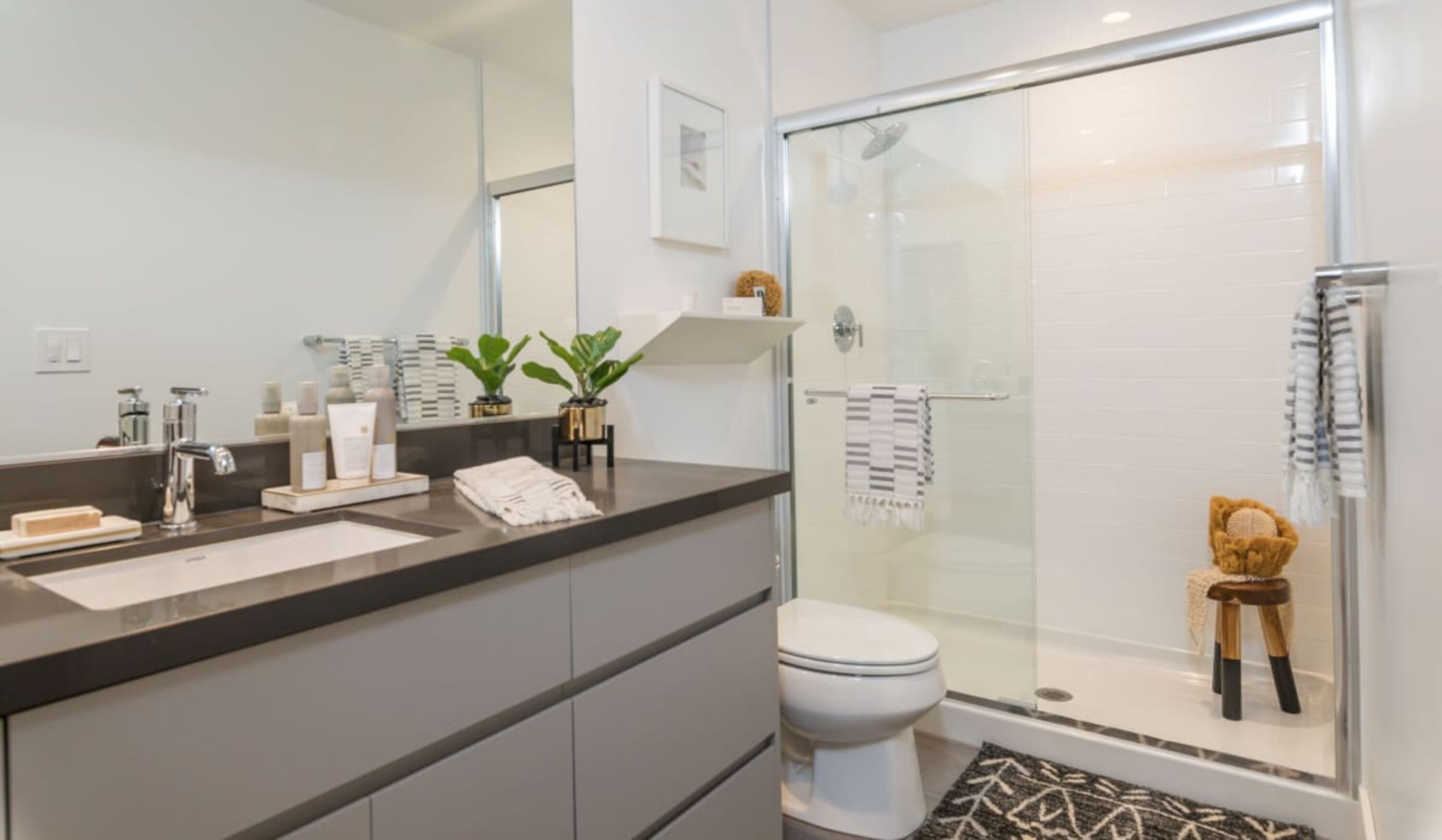 A modern bathroom with a glass-enclosed shower, a large mirror, and a vanity with toiletries.