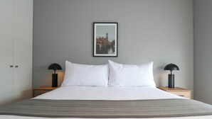 A neatly made bed with white linens, two bedside tables with black lamps, and a framed picture of a building on the wall. - w* | Elegant 2BR w/ Great Deco in San Isidro (San Isidro)