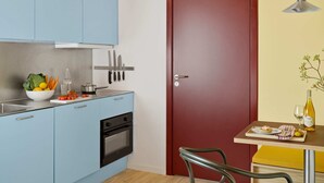 A modern kitchen with light blue cabinets, a red door, and a dining area with a table and chairs. - Cozy Studio Apartment for 2 (København)