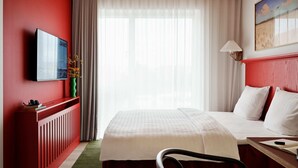Ein Hotelzimmer mit Bett, Schreibtisch, Stuhl, Fernseher und einem Fenster mit Vorhängen.