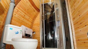 A wooden cabin bathroom with a toilet, a shower enclosure, and a visible water pipe.