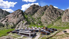 A mountain lodge with yurts and modern buildings, surrounded by rocky terrain and greenery.
