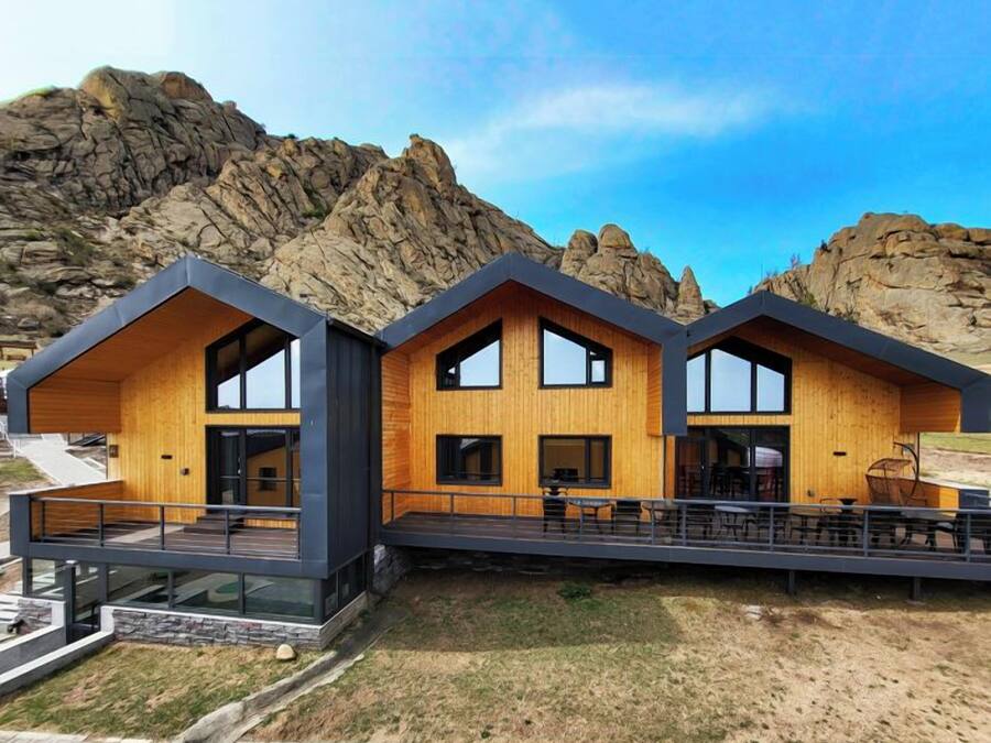 A modern building with a wooden facade and large windows, set against a mountainous backdrop.