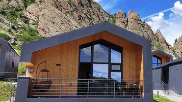 A modern cabin with a large window, a balcony, and a wooden exterior.