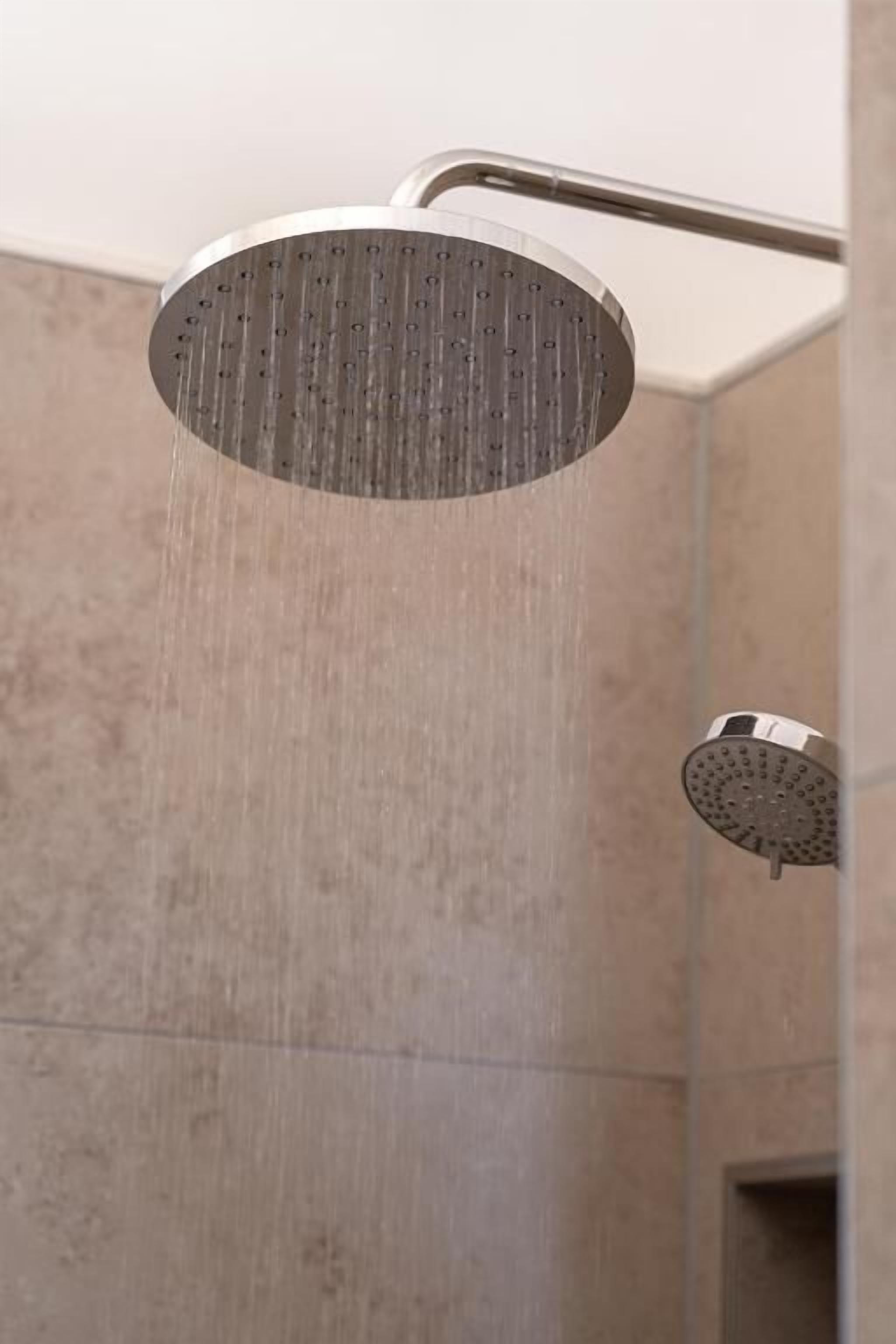 A showerhead with water flowing down, mounted on a wall in a bathroom with tiled walls.