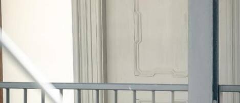 A view of a balcony with a metal railing, a white door with decorative molding, and a plain wall in the background.