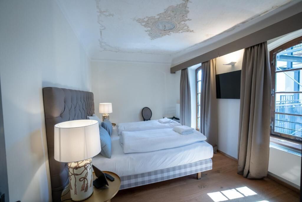 Habitación de hotel con cama, lámpara de noche, espejo y ventana con cortinas.