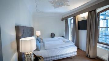 Habitación de hotel con cama, lámpara de noche, espejo y ventana con cortinas.