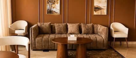 A modern hotel lobby with a sectional sofa, two armchairs, a round wooden coffee table, and a marble floor.
