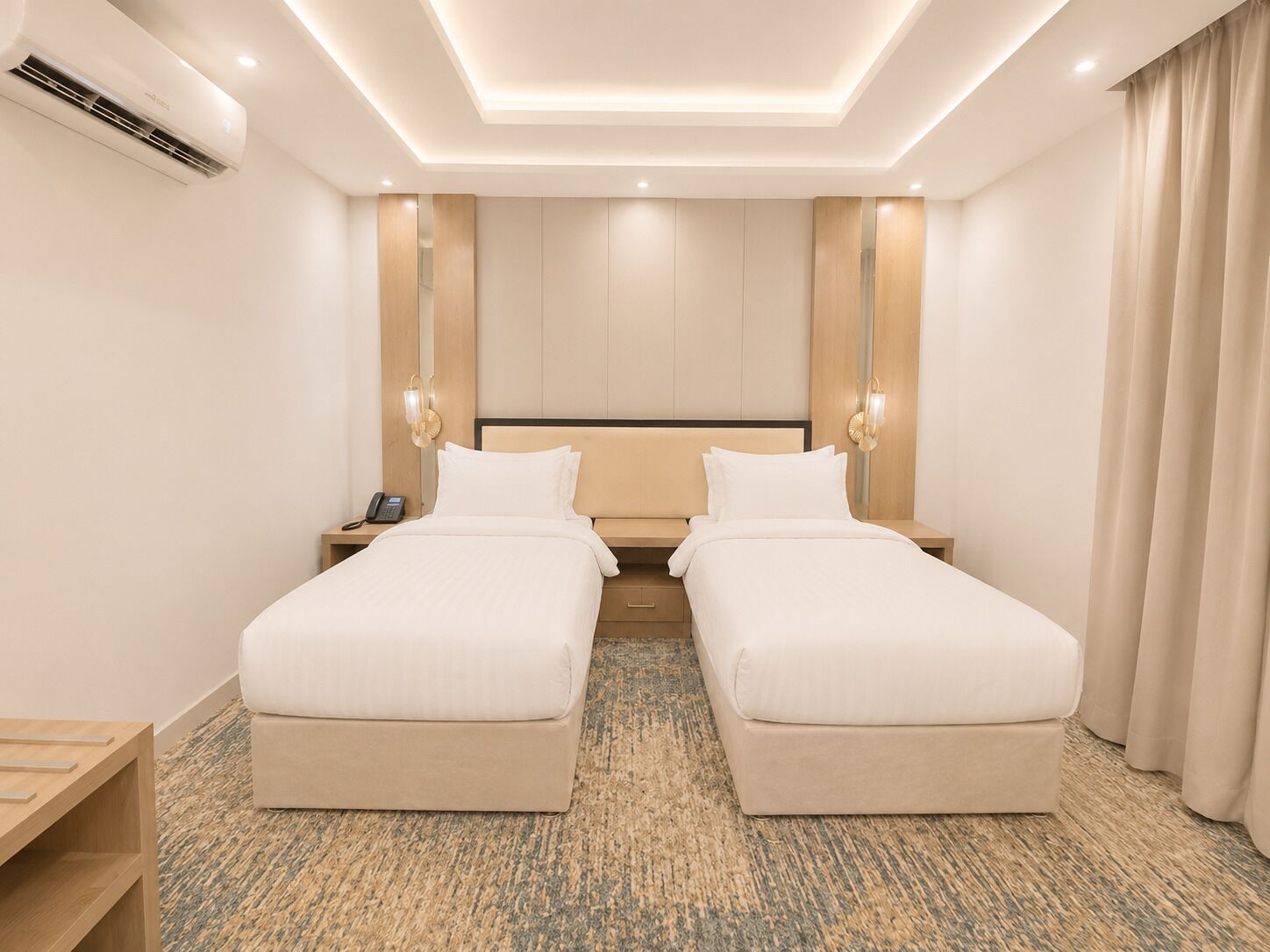 Habitación de hotel con dos camas, una mesita de noche con teléfono, aire acondicionado de pared y alfombra estampada.