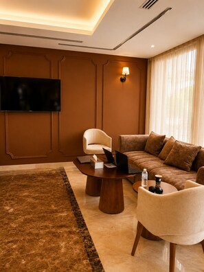 A modern living room with a flat-screen TV, a sofa, a coffee table, and a chair. - Jwana Hotel (Riyadh)