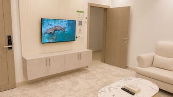 Ein modernes Wohnzimmer mit einem flachbildfernseher an der Wand, einem beigen Sofa, einem Marmor-Couchtisch mit Fernbedienung und einem Holzschrank.