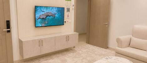 Una sala de estar moderna con un televisor de pantalla plana montado en la pared, un sofá color beige, una mesa de centro de mármol con un control remoto y un armario de madera.
