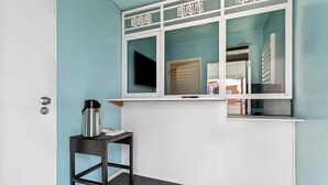 Une pièce avec un mur de couleur turquoise, une fenêtre ornée de moulures décoratives, une table noire avec une bouilloire et une porte.