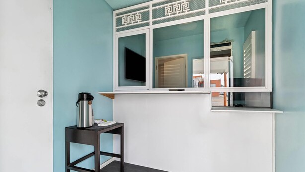 A room with a teal wall, a window with decorative trim, a black table with a kettle, and a door. - Rodeway Inn & Suites North Hollywood Burbank Airport - Universal Area (North Hollywood)