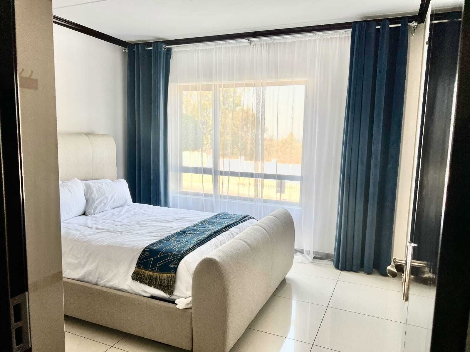 A bedroom with a bed, a window with curtains, and a door.