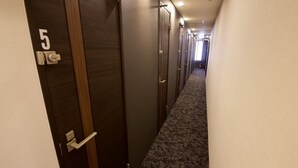 Pasillo de hotel con puertas numeradas 5, 6 y 7, pisos alfombrados y una lámpara en el techo.