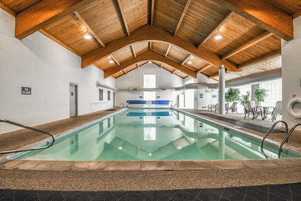 Une piscine intérieure dotée d’un haut plafond en bois, de murs en verre transparent et d’un espace détente avec des tables et des chaises.