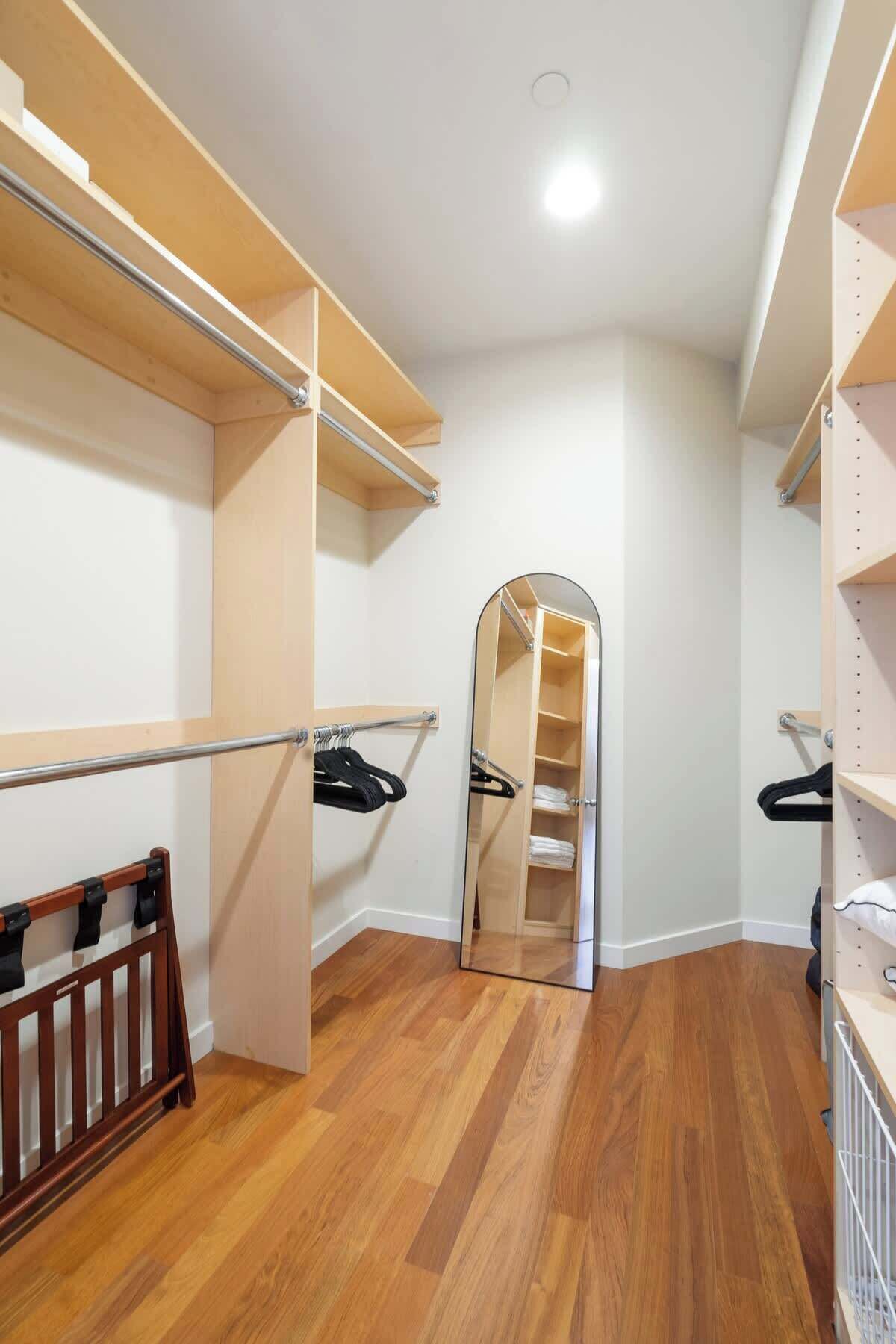 A walk-in closet with wooden flooring, metal rods for hanging clothes, and a mirrored closet door.