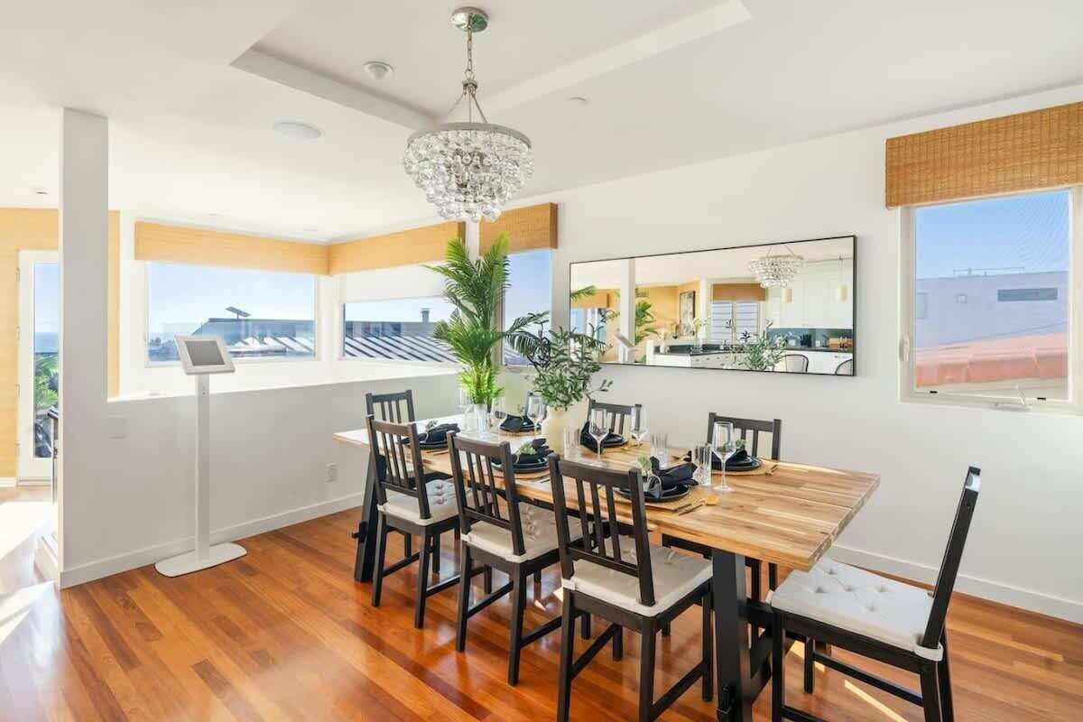 A dining area with a wooden table and chairs, a chandelier, and a large window with a view of the city.