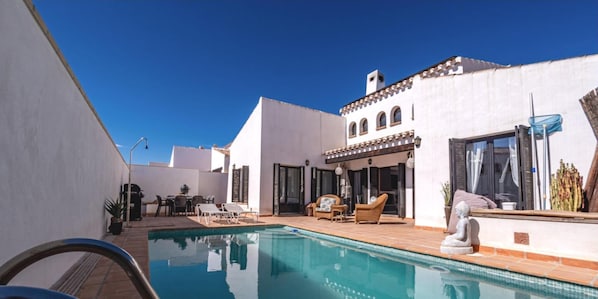 A poolside area with a white building, outdoor furniture, and a statue.