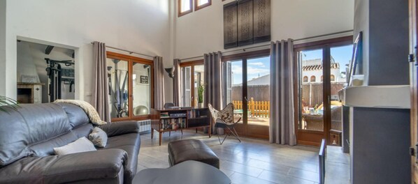 A spacious living room with a leather sofa, a dining table, and a chair. There is a sliding glass door leading to an outdoor area with a view of a building. - Luxury Villa With Private Pool (Murcia)