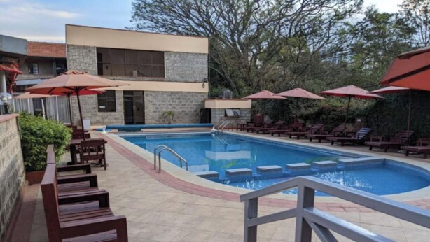 A swimming pool with lounge chairs and umbrellas, surrounded by a stone building and trees. - Bliss Haven (Nairobi)