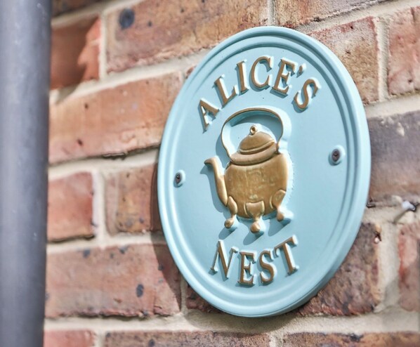 A sign with a brass teapot and the words "ALICE'S NEST" mounted on a brick wall. - Newly Refurbished Flat With Great Transport Links (London)
