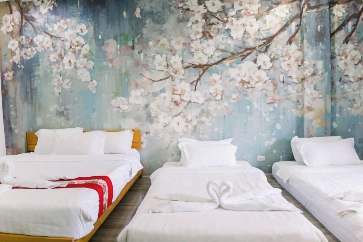 A hotel room with three beds, white bedding, and a wall mural of cherry blossoms.