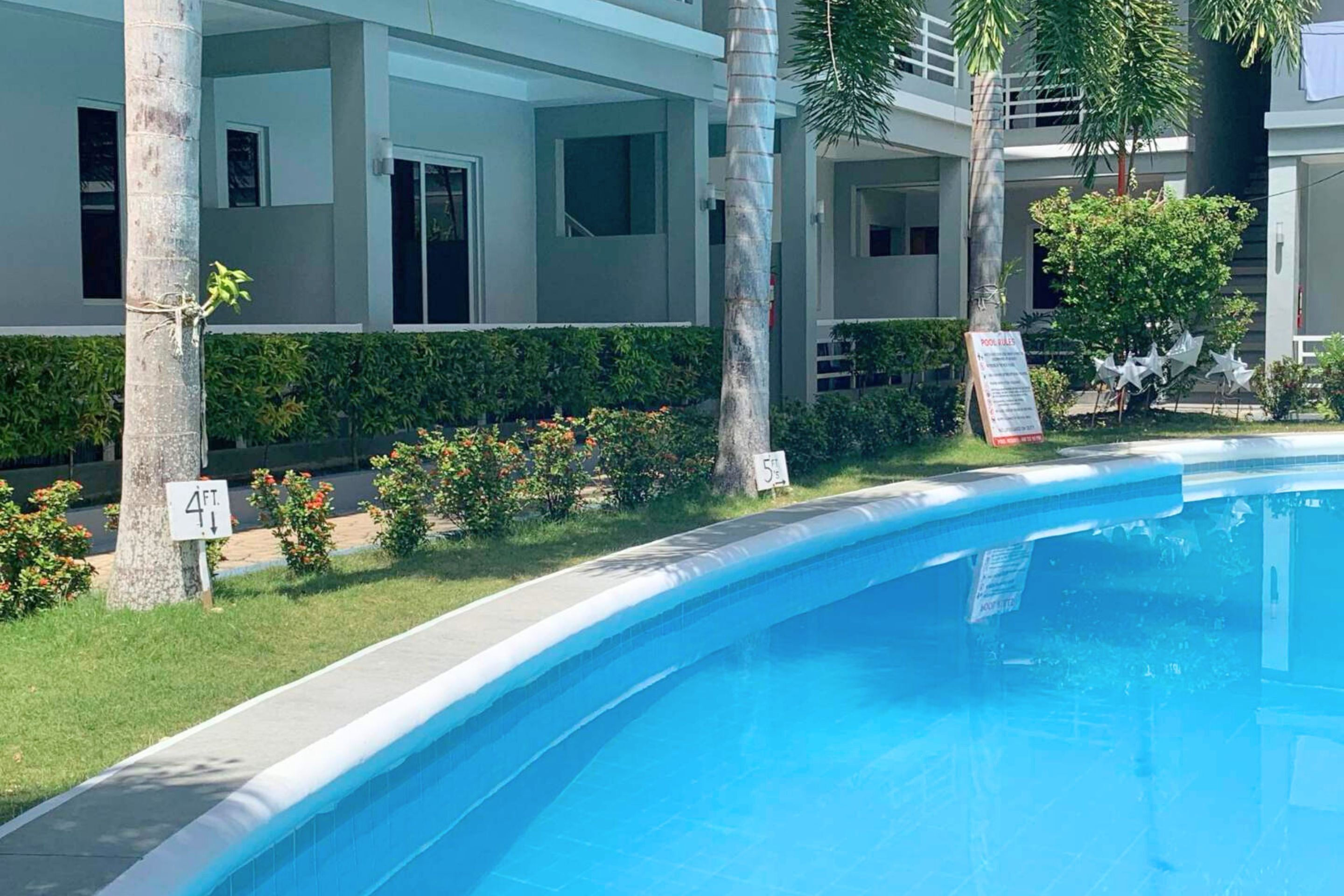 Uma piscina com superfície de água azul cristalina, rodeada por um relvado bem cuidado e um edifício com várias janelas e varandas.