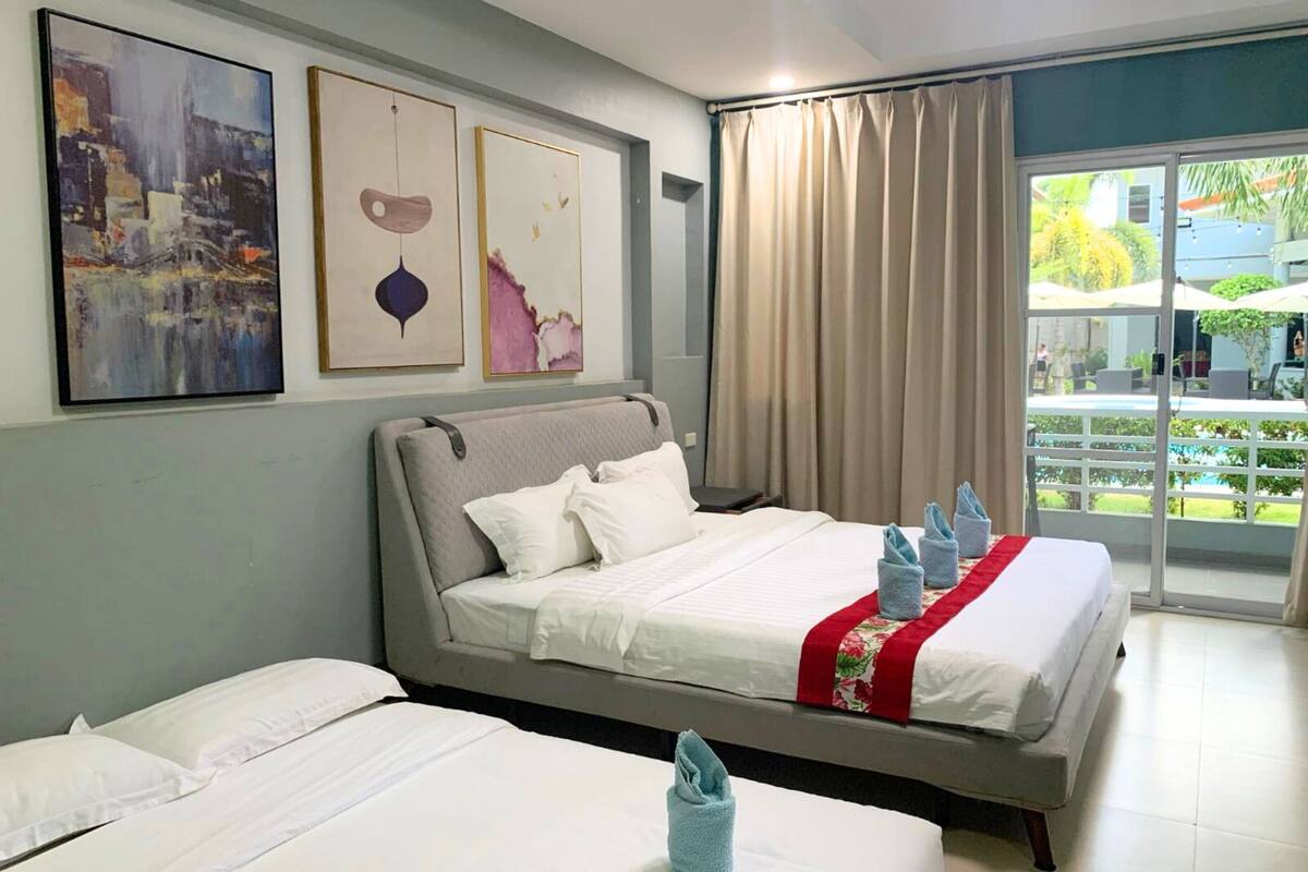 A hotel room with a large bed, two smaller beds, a balcony with a view, and artwork on the wall.