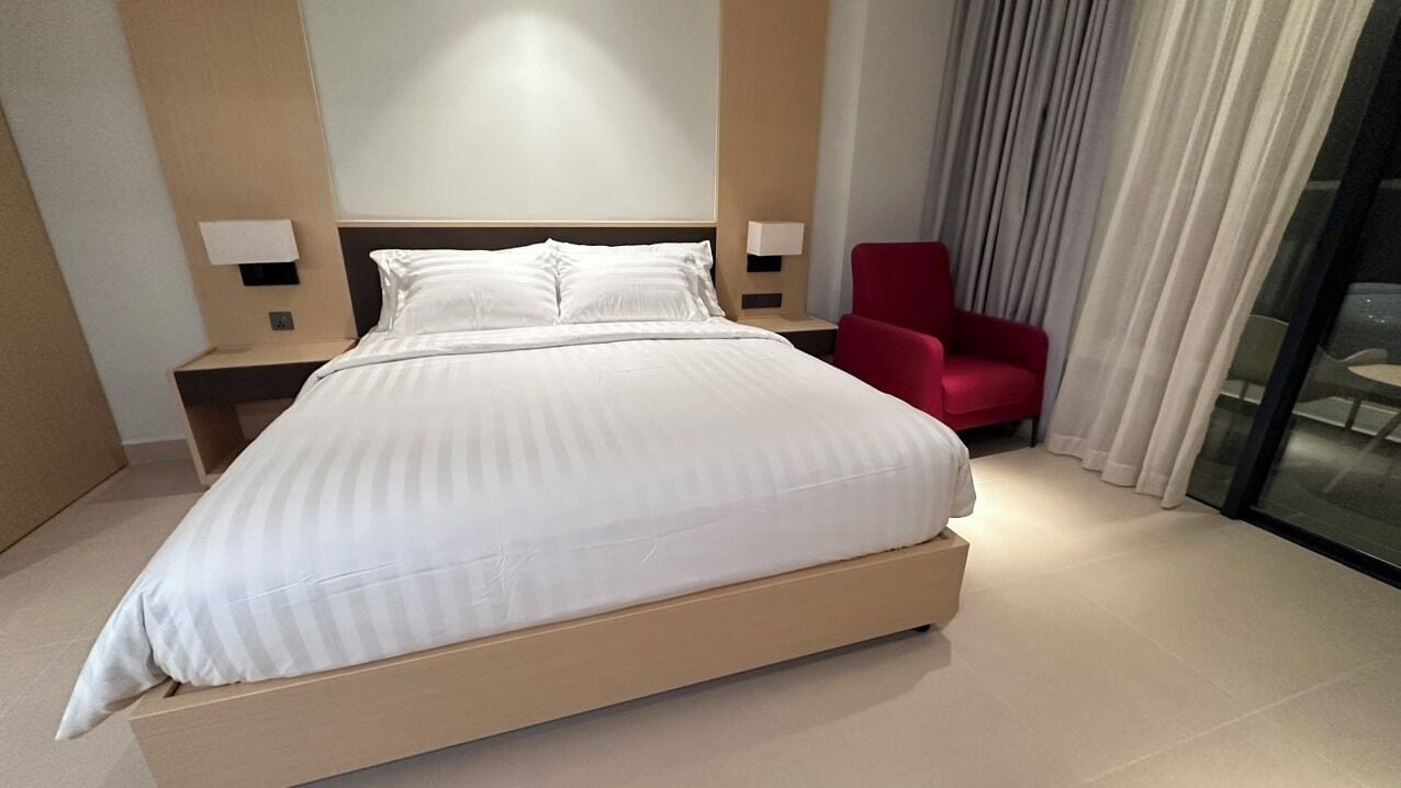 Ein modernes Hotelzimmer mit einem großen Bett, einem roten Sessel und einer Glastrennwand.
